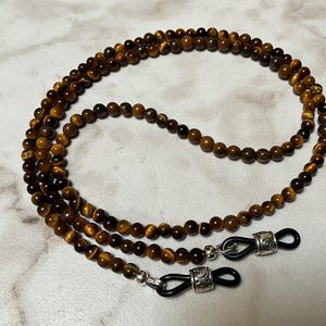 May include: A brown and gold tiger's eye beaded glasses chain with silver clasps.