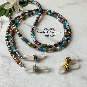 May include: Odyssey beaded eyeglass holder with a multi-colored bead design. The holder features a mix of blue, green, brown, and purple beads. Includes two pairs of eyeglass holders, one with silver and one with gold accents.