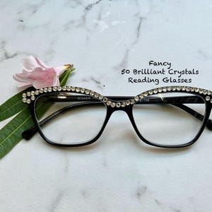 May include: Black reading glasses with a crystal-studded frame. The glasses have a cat-eye shape and clear lenses. The text on the image reads "Fancy 50 Brilliant Crystals Reading Glasses."