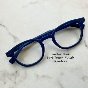 May include: Harbor Blue readers with a soft touch finish. The glasses have a round frame and are made in China. The text on the image reads "Harbor Blue Soft Touch Finish Readers."