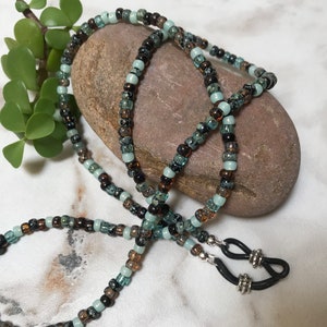 May include: A beaded eyeglass chain with brown, black, and light blue beads. The chain has silver-toned clasps and black rubber ends.