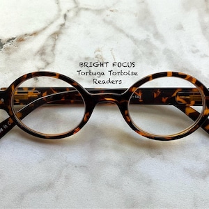 May include: Round-framed reading glasses with a tortoise shell pattern. The glasses have a dark brown and amber color scheme. The text "BRIGHT FOCUS Tortuga Tortoise Readers" is printed above the glasses. The glasses are made in China.
