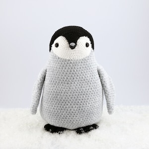 Puede incluir: Un animal de peluche de ping&uuml;ino tejido a crochet con un cuerpo gris y una cabeza negra. El ping&uuml;ino tiene ojos blancos y un pico negro.