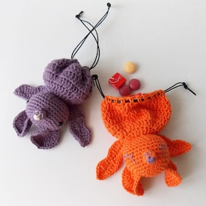 May include: Two crocheted bunny-shaped drawstring bags. One is purple and the other is orange. Both bags have black drawstrings.
