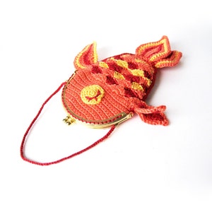 May include: A crocheted purse shaped like a red and yellow fish with a gold clasp. The purse has a red strap.