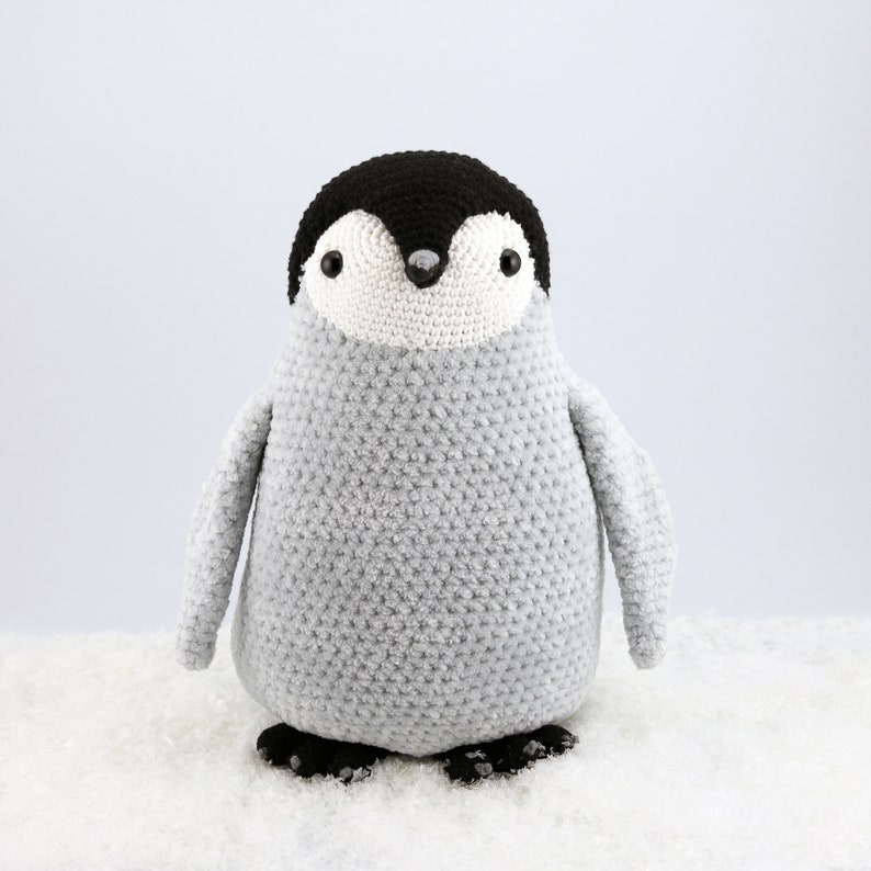 Puede incluir: Un animal de peluche de ping&uuml;ino tejido a crochet con un cuerpo gris y una cabeza negra. El ping&uuml;ino tiene ojos blancos y un pico negro.
