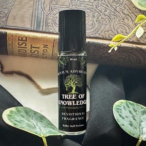 May include: A black rollerball perfume bottle with the text "Tree of Knowledge" and "Devotional Fragrance". The bottle is 10 ml and is set against a backdrop of a book and greenery.