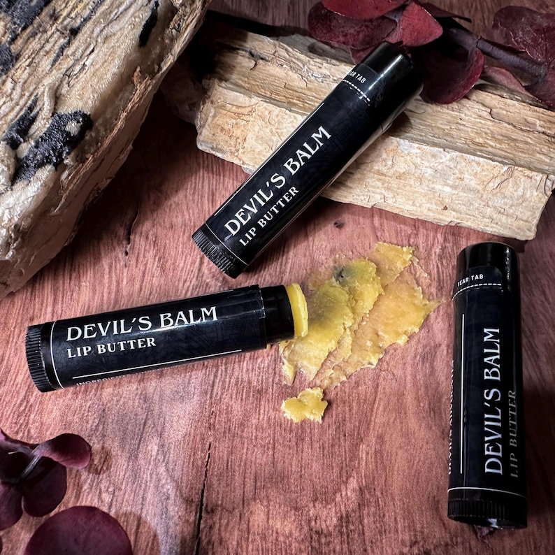 May include: Two black lip balm tubes with the text "Devil's Balm Lip Butter" on them. The balm is yellow and has been partially used.