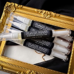 May include: Five clear plastic tubes with black labels that read "Black Mass Scented Cuticle Oil" and "3 ML / 0.1 FL OZ". The tubes are arranged in a gold picture frame.
