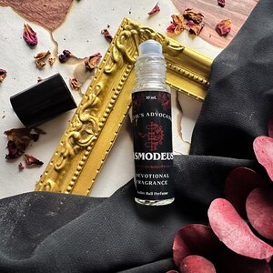 May include: A 10 ml roller ball perfume bottle with a black and red label. The label reads "Devil's Advocate", "Asmodeus", "Devotional Fragrance", and "Roller Ball Perfume".