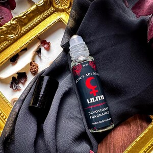 May include: A black and red rollerball perfume bottle with the text "Devil's Advocate Lilith Devotional Fragrance Roller Ball Perfume" and a crescent moon and female symbol.