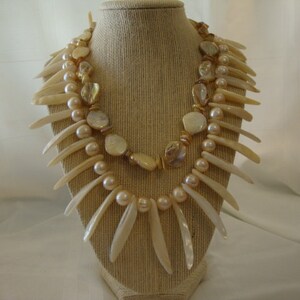 May include: A two-strand necklace with a variety of white and cream-colored shell beads and a long, pointed, white shell fringe.