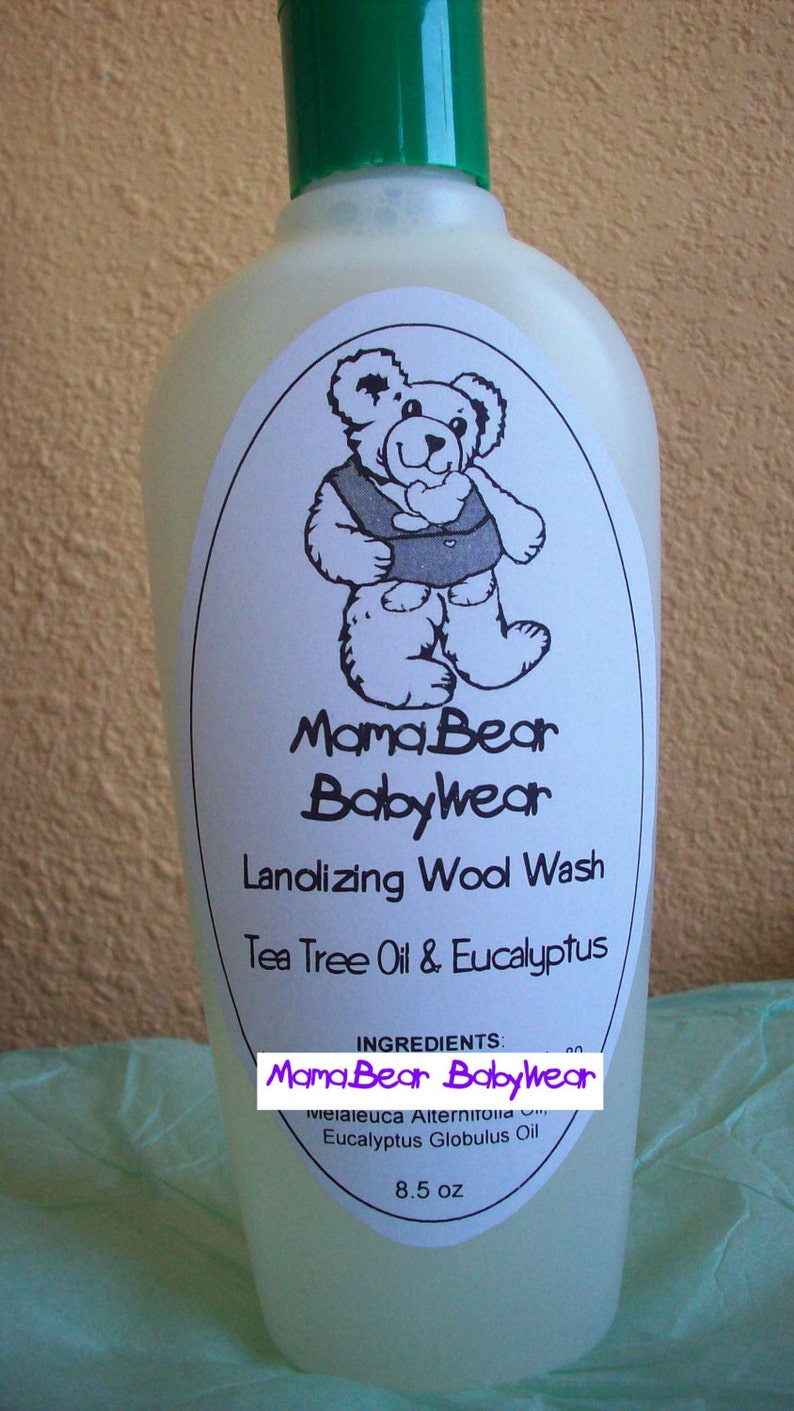 May include: A clear plastic bottle with a green lid and a white label. The label features a cartoon bear wearing a bib and the text "Mama Bear Babywear Lanolizing Wool Wash Tea Tree Oil & Eucalyptus". The ingredients are listed on the label: "Melaleuca Alternifolia Eucalyptus Globulus Oil". The bottle contains 8.5 ounces of liquid.