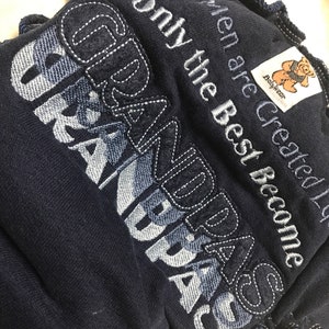 Könnte beinhalten: Ein dunkelblauer Baby-Strampler mit weißen Nähten. Der Strampler hat die Worte "When are created only the best become GRANDPAS" aufgestickt. Der Strampler hat ein kleines Etikett mit einem Bärenlogo, auf dem "Babywear" steht.