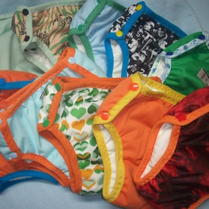 May include: A collection of colorful cloth diapers with various patterns, including animal prints, hearts, and abstract designs. The diapers have contrasting colored trim and snap closures.