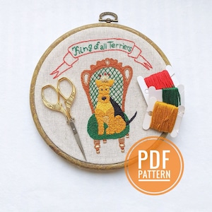 May include: Embroidered hoop art featuring a wirehaired terrier dog wearing a crown, sitting on a throne with the text "King of all Terriers" above. The hoop is surrounded by embroidery floss in red, green, and yellow.