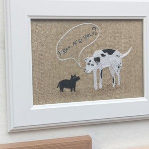 May include: Embroidered artwork on burlap fabric in a white frame. The artwork features two dogs, one black and one white with black spots, with a speech bubble above the white dog that says "How are you?"