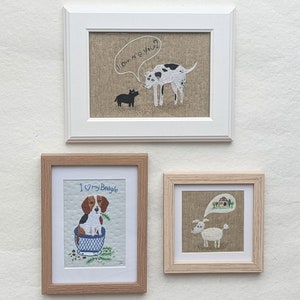 May include: Three framed embroidery pieces featuring dogs. The top frame shows a black and white dog with a speech bubble saying "How are you?" The middle frame shows a beagle in a blue cup with the text "I &hearts; my Beagle". The bottom frame shows a white dog with a speech bubble showing a house.