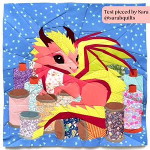 Può includere: Una colorata trapunta geometrica raffigurante un drago rosa con ali gialle e rosse, circondato da rocchetti di filo. Lo sfondo è blu con stelle bianche, e il testo "Test pieced by Sara @sarabquilts" è visibile.
