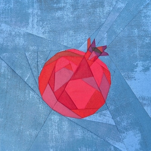 May include: A fabric quilt block featuring a geometric pomegranate design constructed from various shades of red and pink fabric pieces. The pomegranate is set against a background of blue fabric strips with a mottled, textured appearance.