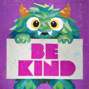 May include: A colorful quilt featuring a geometric monster holding a sign that reads "BE KIND." The monster is primarily green and blue with yellow eyes and orange horns. The sign is white with pink lettering, set against a purple background.