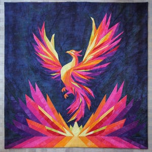 May include: A vibrant, geometric quilt featuring a phoenix rising against a dark blue background. The bird is rendered in shades of pink, orange, and yellow, with outstretched wings and a stylized tail. The quilt's design includes a burst of color at the bottom.