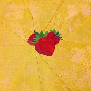Peut inclure: Un bloc de courtepointe carré en tissu présentant un groupe central de trois fraises rouges avec des feuilles vertes. Les fraises sont entourées d'un motif en rayons de soleil composé de pièces de tissu jaune à la texture marbrée.