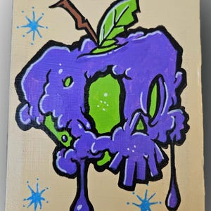 May include: A hand-painted artwork on a rectangular wooden panel. The image features a stylized purple apple with a green center and black outlines. Blue starbursts and dripping purple paint add detail. A brown stem and green leaf complete the design.