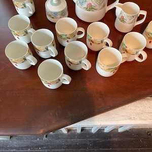 May include: A white tea set with a floral design. The set includes a teapot, creamer, sugar bowl, and 12 teacups.