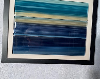 Könnte beinhalten: Abstrakte gerahmte Kunst mit horizontalen Farbstreifen in Blau- und Gelbtönen. Das Kunstwerk ist in einem schwarzen Rahmen und einem weißen Passepartout gefasst. Das Kunstwerk ist an einer strukturierten weißen Wand montiert.