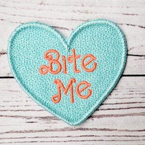 May include: A light blue heart-shaped patch with the words "Bite Me" embroidered in orange.