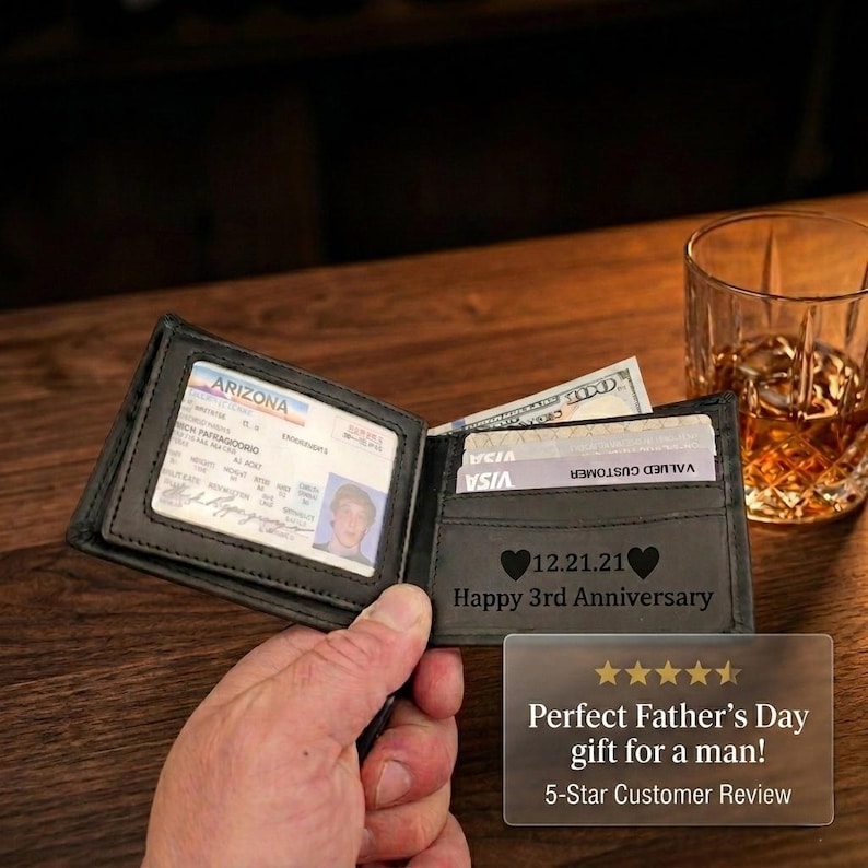 May include: A black leather bifold wallet featuring a clear ID window containing an Arizona driver license and a card slot section engraved with the text 12.21.21 Happy 3rd Anniversary, flanked by two heart icons, with visible credit cards.