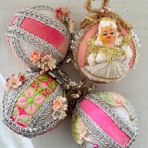 May include: Four vintage Christmas ornaments. Two ornaments have pink velvet stripes, silver trim, and floral accents. One ornament features an angel with gold glitter wings. The fourth ornament has pink and green floral embroidery.