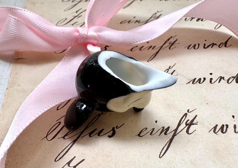 K&ouml;nnte beinhalten: Kleine, schwarz-wei&szlig;e Keramik-Orca-Wal-Figur mit wei&szlig;em Innenraum. Die Figur befindet sich auf einem Vintage-Papierhintergrund mit Kursivschrift und einem rosa Band.