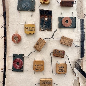 May include: A collection of vintage electronic components, including copper wire coils, rectangular capacitors, and metal plates, arranged on a weathered paper sheet with the handwritten name Nellie Nelson at the top. Various parts feature printed text.