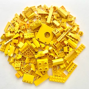May include: A large collection of assorted yellow plastic building bricks and construction components of various shapes and sizes, including rectangular blocks, flat plates, curved pieces, and specialized elements scattered in a pile.