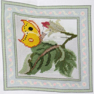 May include: A yellow butterfly with black spots is perched on a green leaf with a white flower. The butterfly and flower are surrounded by a green and white border.