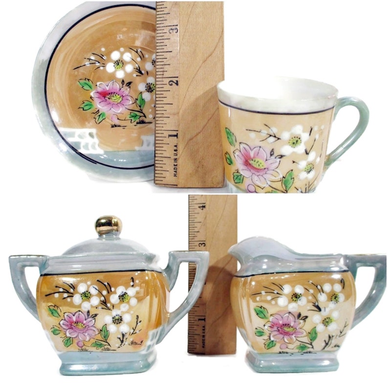 Pode incluir: Um conjunto de ch&aacute; vintage com um design floral. O conjunto inclui um bule, um jarro de creme, um a&ccedil;ucareiro, uma x&iacute;cara e um pires. As pe&ccedil;as s&atilde;o decoradas com flores rosa e brancas sobre um fundo marrom claro.