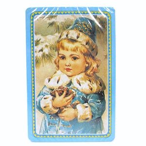 May include: A vintage-style Christmas card featuring a young girl wearing a blue hat and coat, holding a pine cone. The card has a blue border with a yellow and gold pattern.