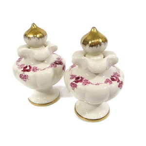 May include: Two white ceramic bottle stoppers with gold accents and pink floral designs.