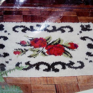 May include: A white rug with a black floral design and red roses. The rug has a black border with a decorative pattern.