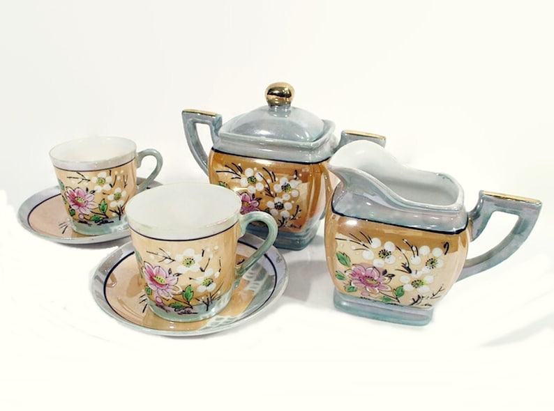 May include: A vintage tea set with a floral design. The set includes a teapot, creamer, and two teacups and saucers. The pieces are made of porcelain and have a light blue and gold glaze.
