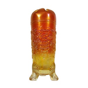 May include: A clear glass vase with a grape design. The vase is a deep amber color with a lighter yellow at the bottom. The vase has three legs and a rounded top.