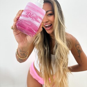 May include: A clear pink bottle with a white pump top and the text "Blow Girl" in pink. The bottle is labeled "Gel Arom&aacute;tico para Banho" and "Hidrata&ccedil;&atilde;o com Creme".