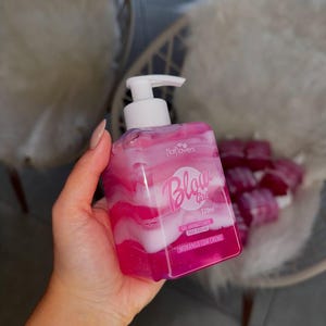 May include: Pink and white bottle of body wash with a pump dispenser. The bottle is labeled "Blow Girl" and "Morango com Creme".