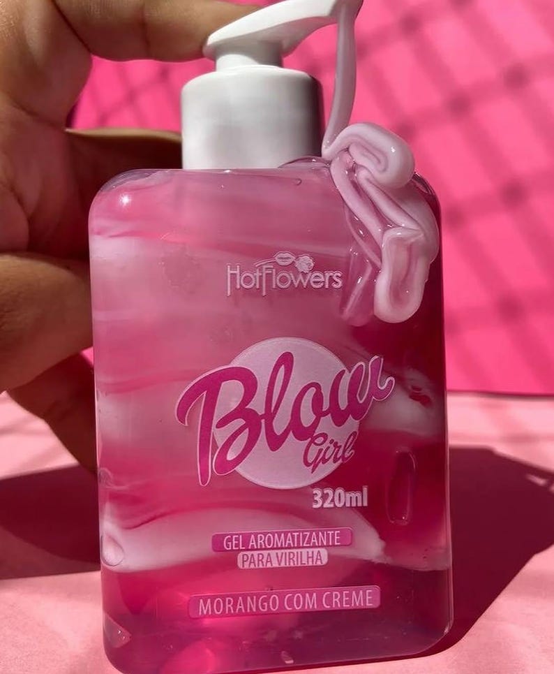 May include: A pink bottle of gel with a white pump top and a white swirl of gel on the side. The bottle is labeled "Blow Girl 320ml Gel Aromatizante Para Virilha Morango Com Creme".