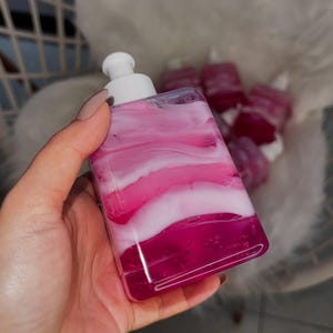 May include: A clear bottle with a white pump dispenser filled with pink and white liquid. The liquid has a marbled appearance.