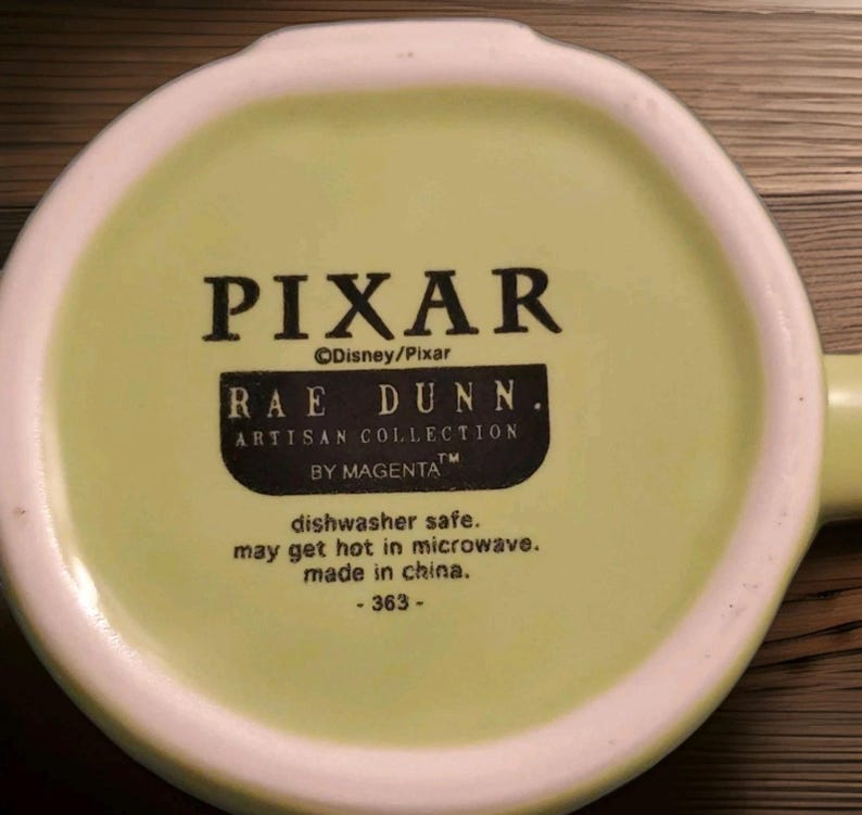 Peut inclure: Le dessous d'une tasse en c&eacute;ramique vert clair avec un texte imprim&eacute; en noir indiquant PIXAR, Disney/Pixar, RAE DUNN. ARTISAN COLLECTION BY MAGENTA, dishwasher safe, may get hot in microwave, made in china, et le num&eacute;ro 363.