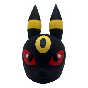 May include: A black Umbreon figure with yellow accents on the ears and a yellow ring on the forehead. The eyes are red with white pupils. The figure is a 3D-printed model of the Pokémon character.
