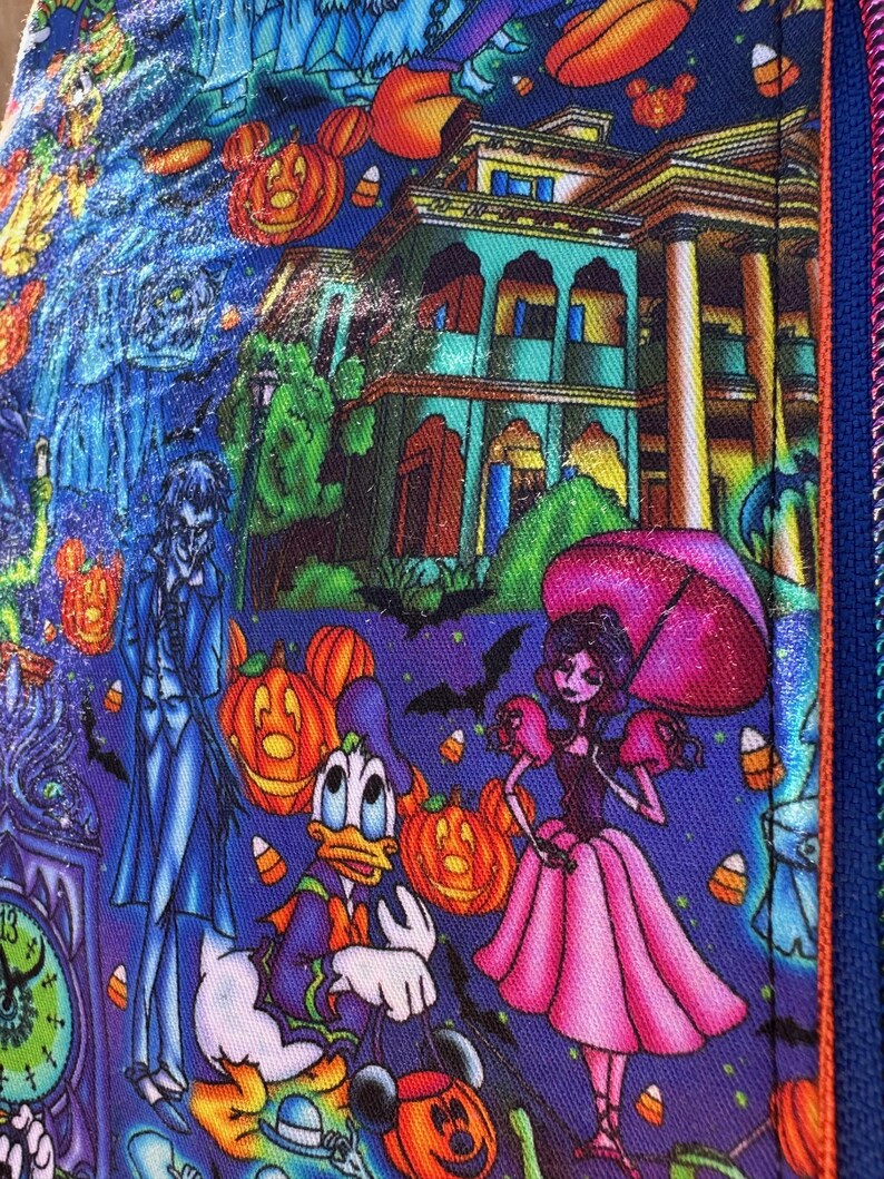 Może przedstawiać: Kolorowa tkanina o tematyce Halloween z postaciami z kresk&oacute;wek, dyniami i nawiedzonym domem. Projekt zawiera Kaczora Donalda, kobietę z r&oacute;żowym parasolem i zegar. Tkanina ma niebieskie tło z pomarańczowymi, fioletowymi i zielonymi akcentami.